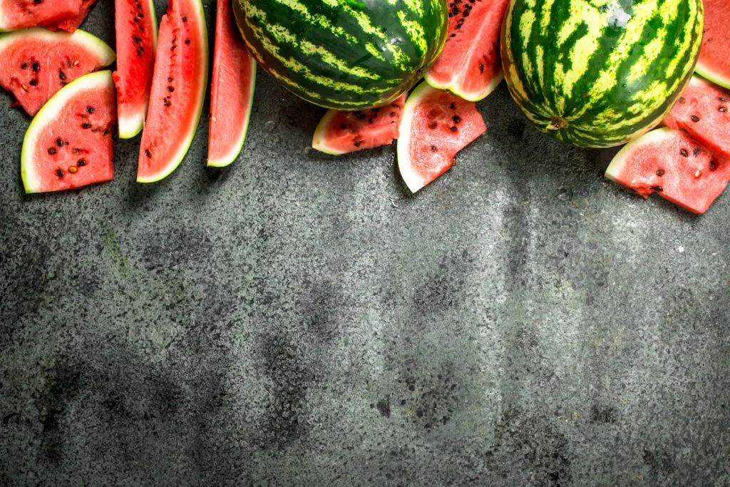Fresh ripe whole and sliced watermelon on black background