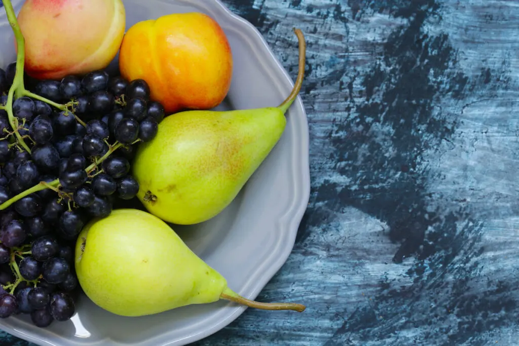 Grapes, Pears, Peaches in white plate blue background 