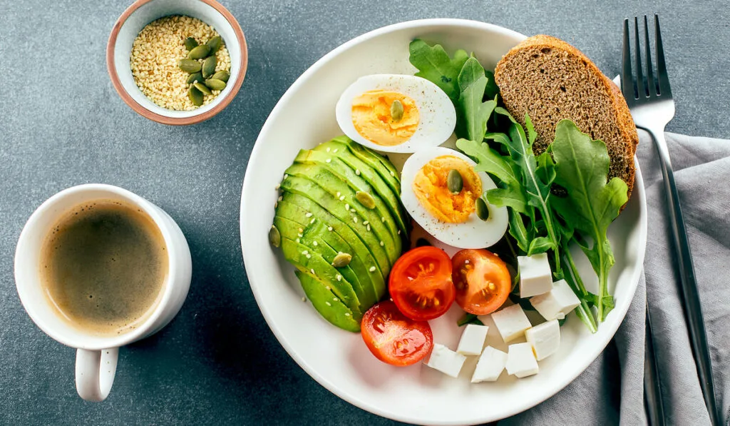 Healthy breakfast bowl. Avocado, egg, tomato, feta cheese,  bread and cup of coffee