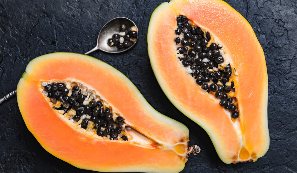 sliced papaya with silver spoon on black concrete background
