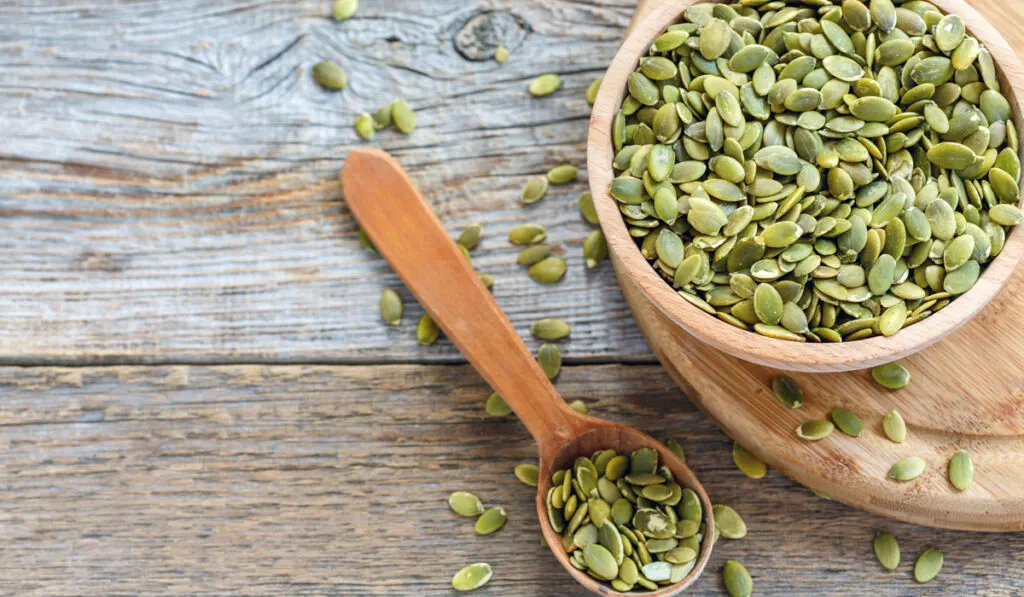 wooden bowl and spoon filled with pumpkin seeds