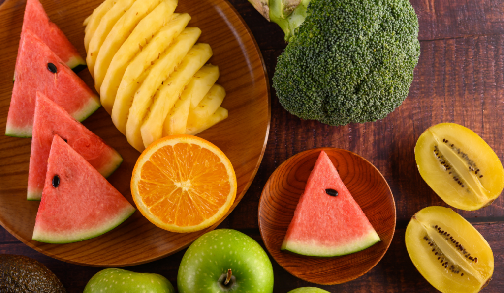 Watermelon, orange, pineapple, kiwi cut into slices with apples and broccoli on a wooden plate.