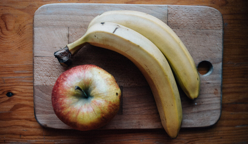 apple and banana on wooden chop board 