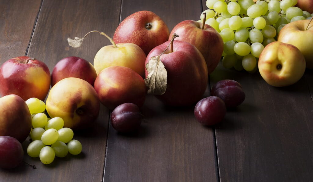 Ripe fresh apples, nectarines, plums and grapes on dark wooden surface