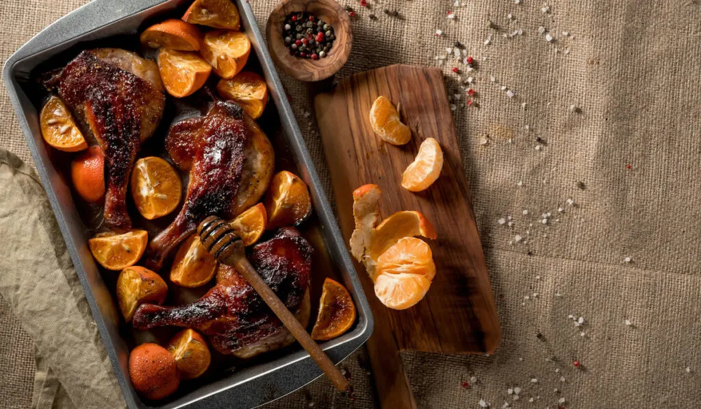 Roast Duck with tangerines and oranges on a baking pan with honey sauce, wooden board with oranges and spices on the background