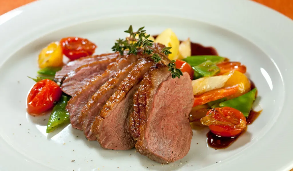 Roasted duck in slices with thyme in port wine sauce, served with cherry tomatoes, sliced potatoes, carrots and asparagus.