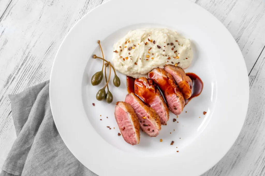Sliced Sous Vide Duck breast with red wine sauce and dip on white plate
