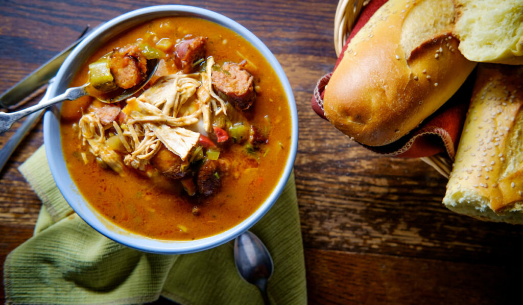 Spicy Duck and andouille sausage Gumbo with fresh crusty bread on a wooden table