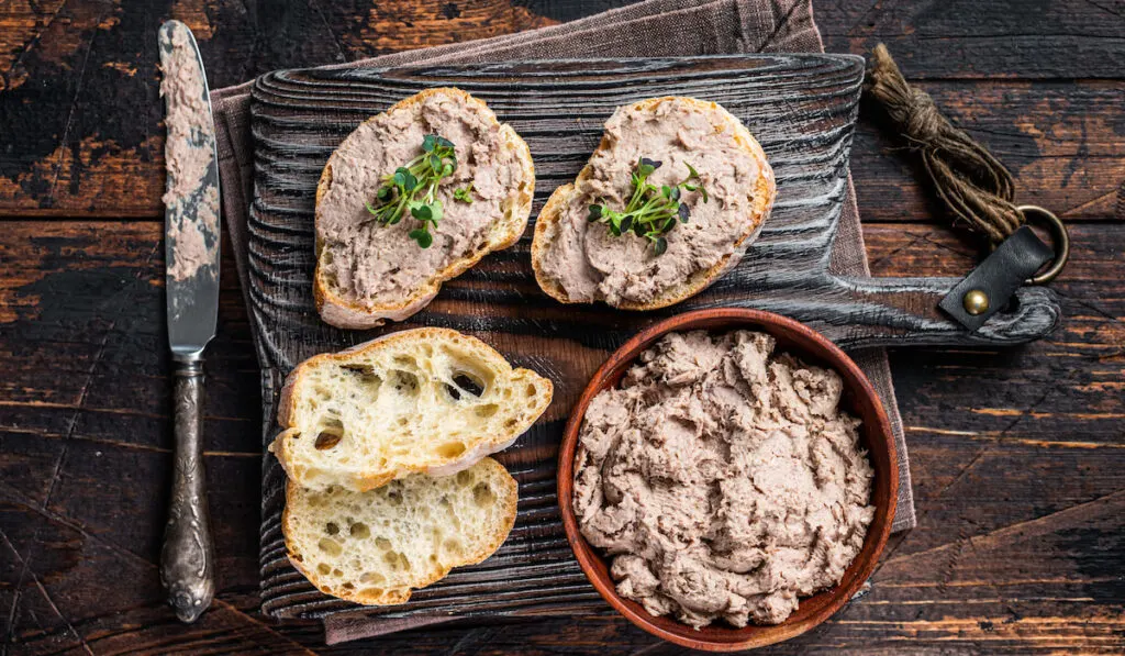 Toasts with Duck pate Rillettes de Canard on wooden board. Dark wooden background