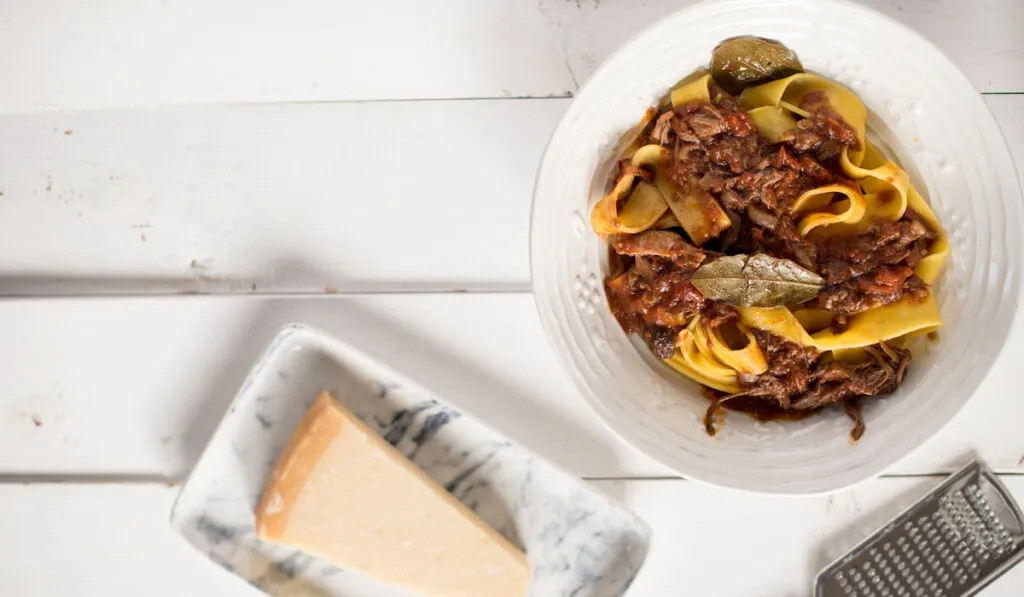 Venetian duck ragu and slice of cheese, fork and cheese grater on white table