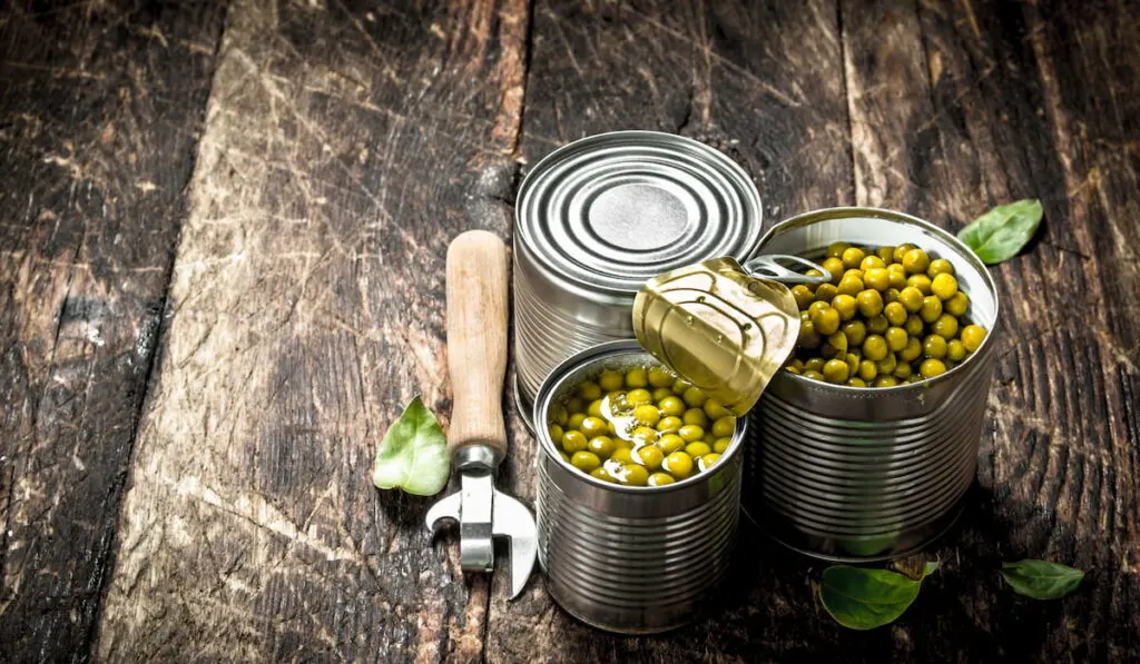 Canned green peas in a tin can with opener, on a wooden background.