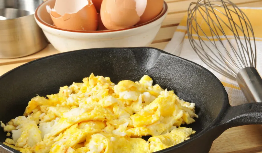 Scrambled eggs with brown egg shells in a bowl behind
