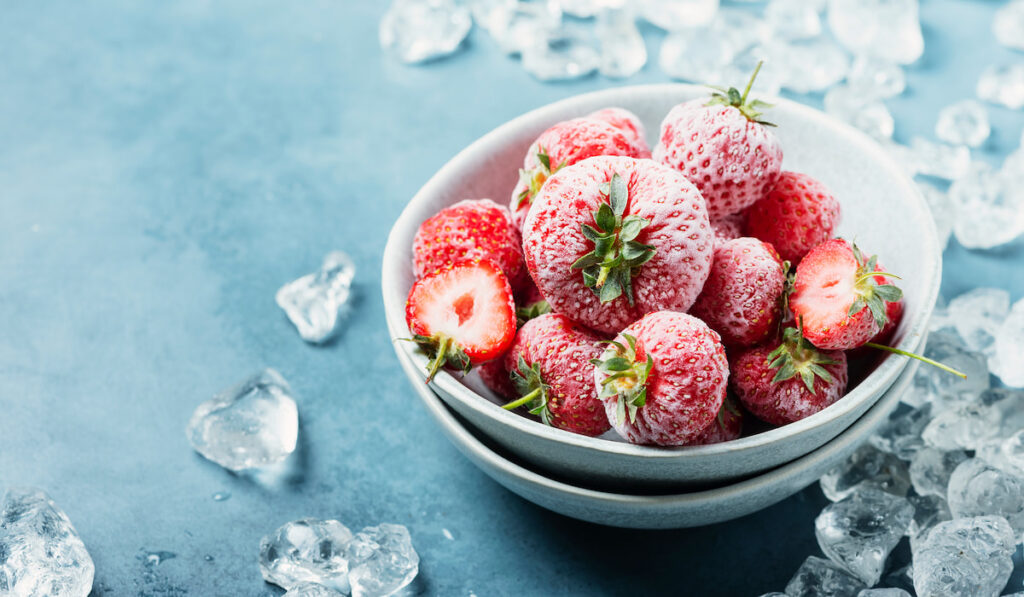 Frozen Strawberry with crystals of ice on blue background