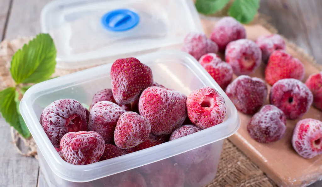 Frozen strawberries in plastic tub on the table