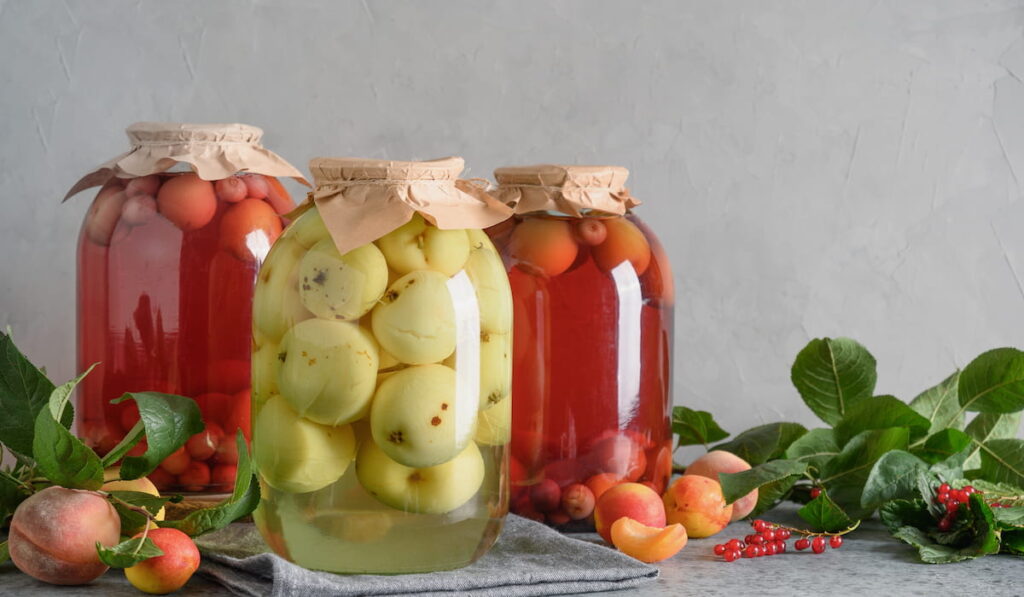 Homemade canned apple and cherry compote in large glass jars on gray tabletop