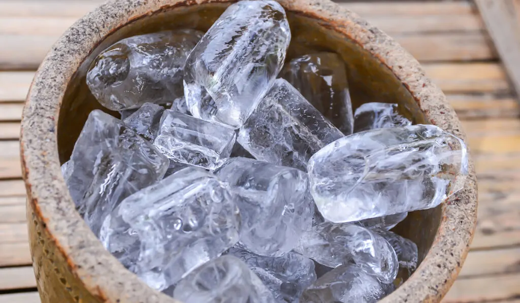 Ice cubes on wooden bucket on texture background 