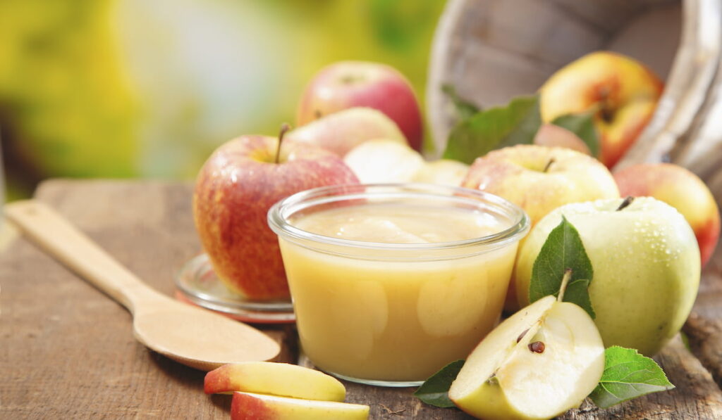 apple sauce in a small glass jar with sliced apple pieces and a wooden spoon on an old wooden table