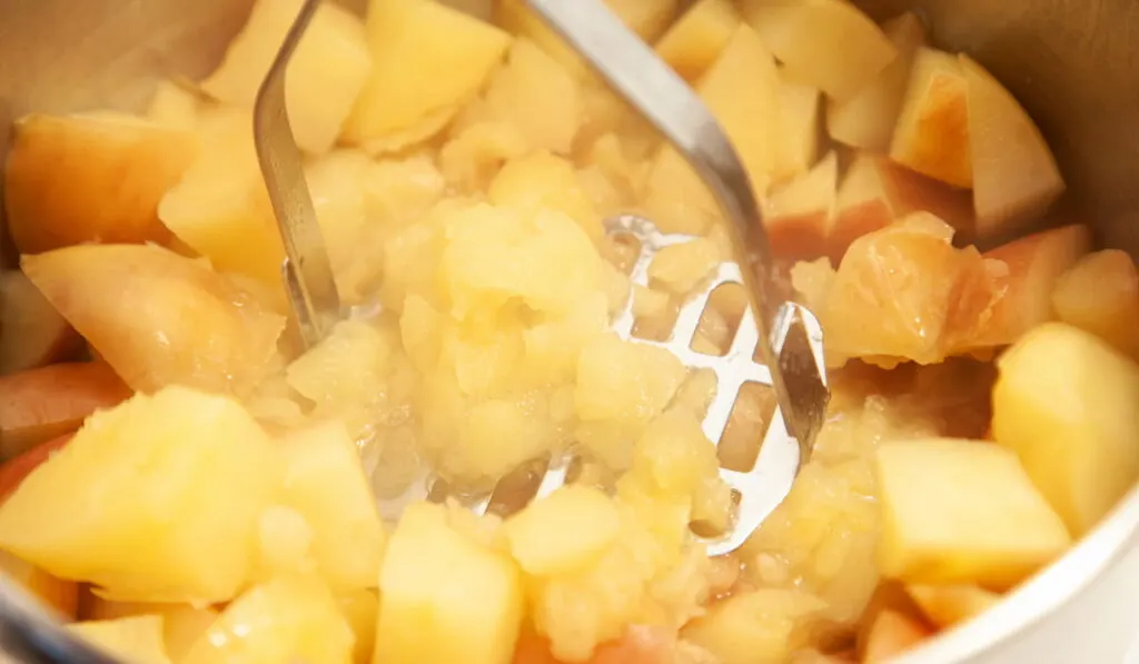 handle of a masher squishes apples together in a steaming pot