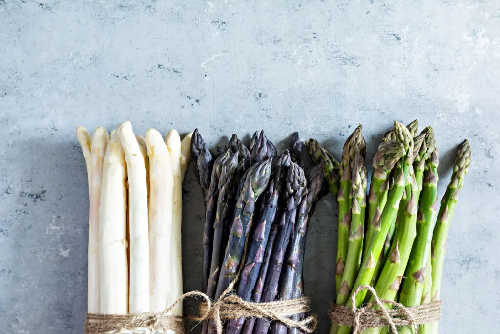 Raw white, purple, green asparagus on a blue background